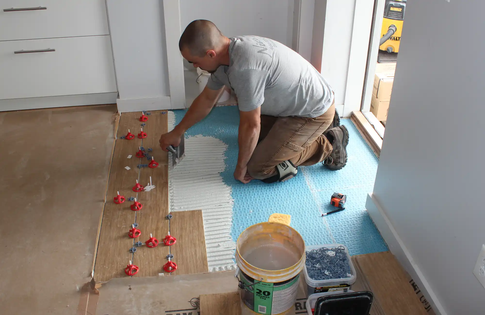 Setting wood-look plank tile with a notched trowel, spacers holding the joints true